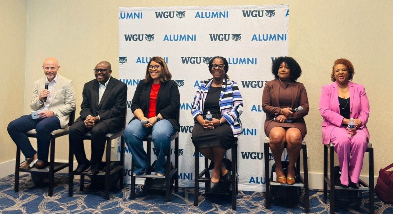 Six diverse individuals, two men and four women, smiling and sitting on a panel in front of a WGU Alumni banner.